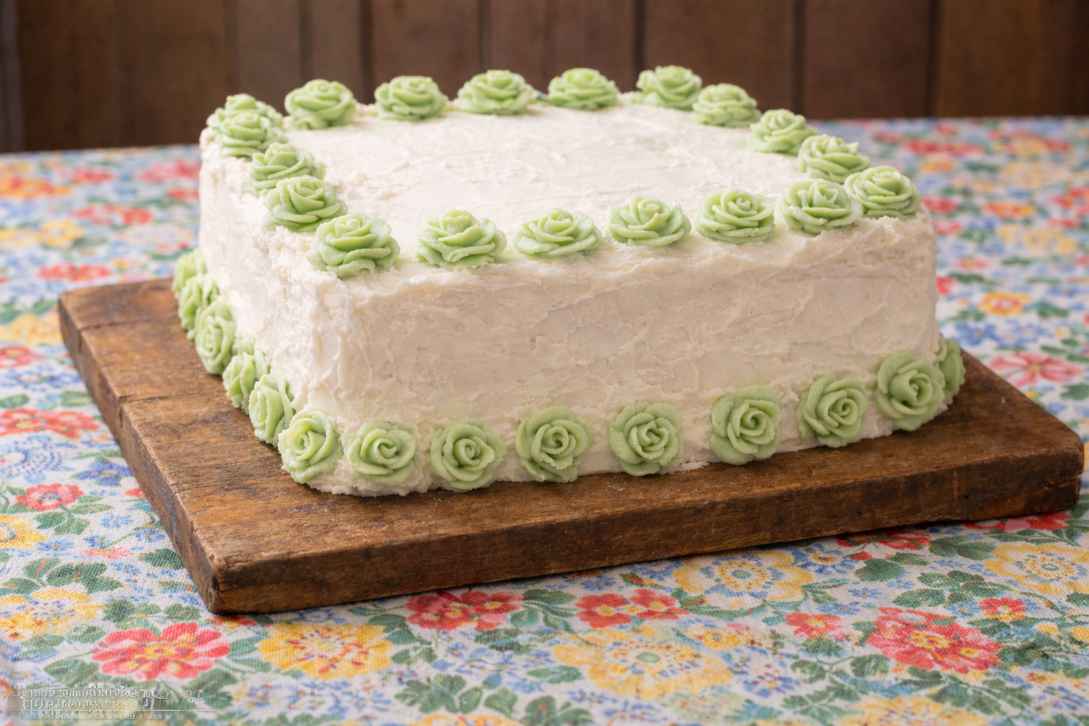 bolo de aniversário antigo quadrado com glacê branco e flores de açúcar verdes sobre tábua de madeira.